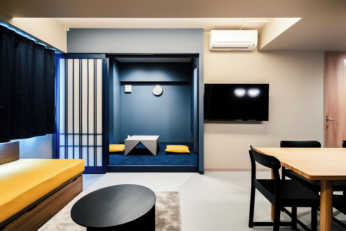 Una sala de estar moderna con sofá, una mesa de centro, un televisor montado en la pared y una zona de comedor con mesa y sillas.