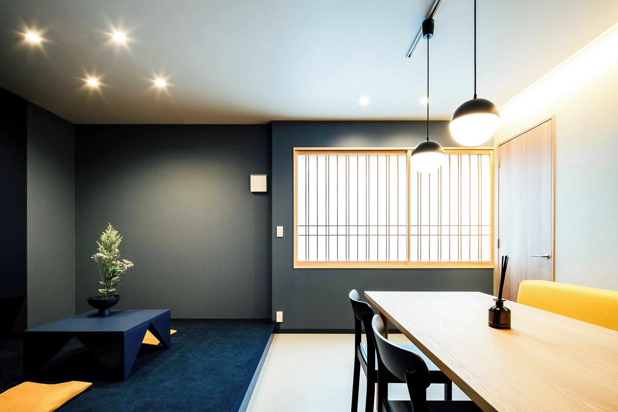 A modern interior with a dining area, a blue carpet, a potted plant, and a window with vertical blinds.