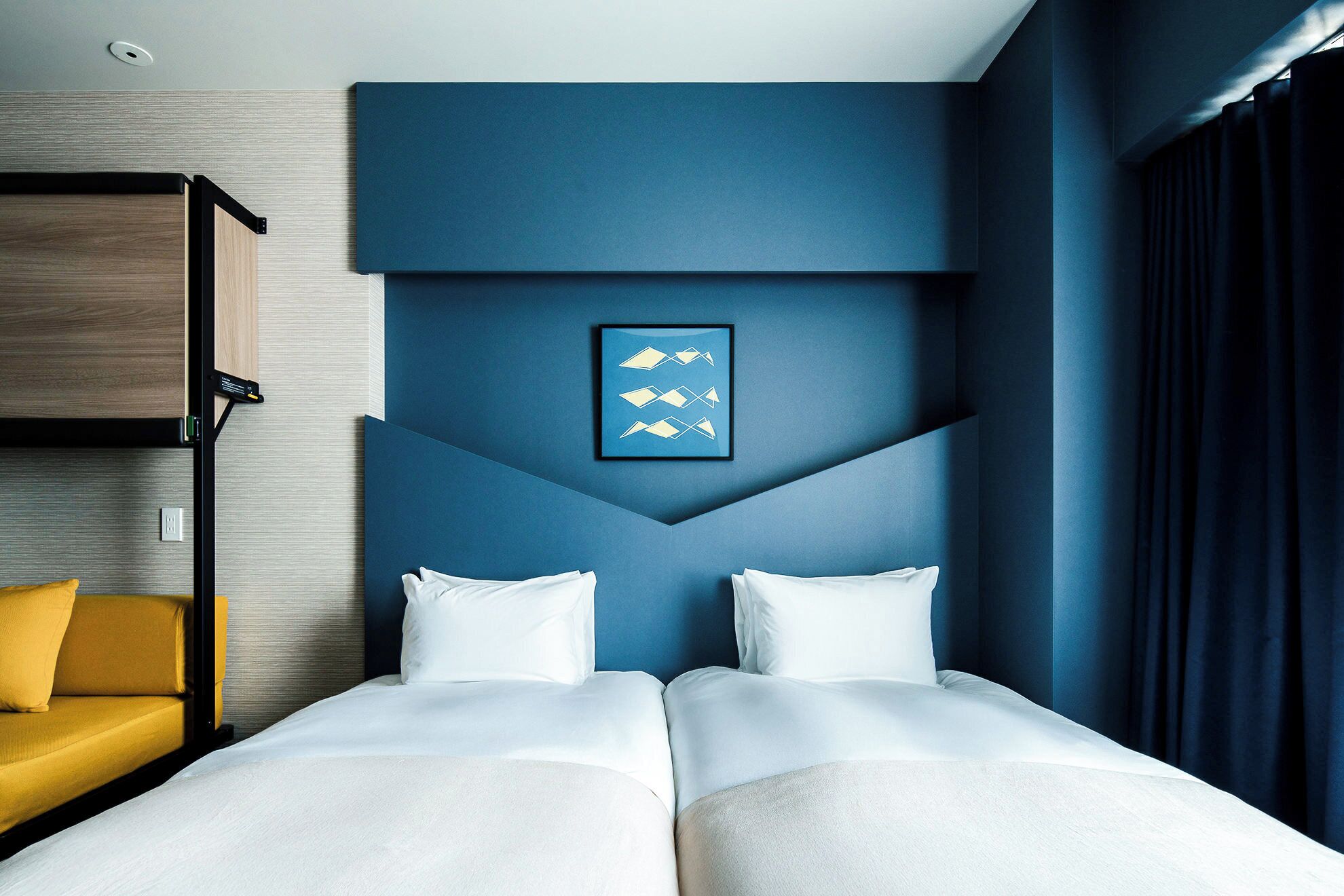 A hotel room with a bed, a yellow chair, and a framed picture on the wall.