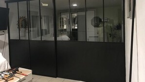 A room with a sliding glass door, a bed with a white comforter, and a small table with tools.