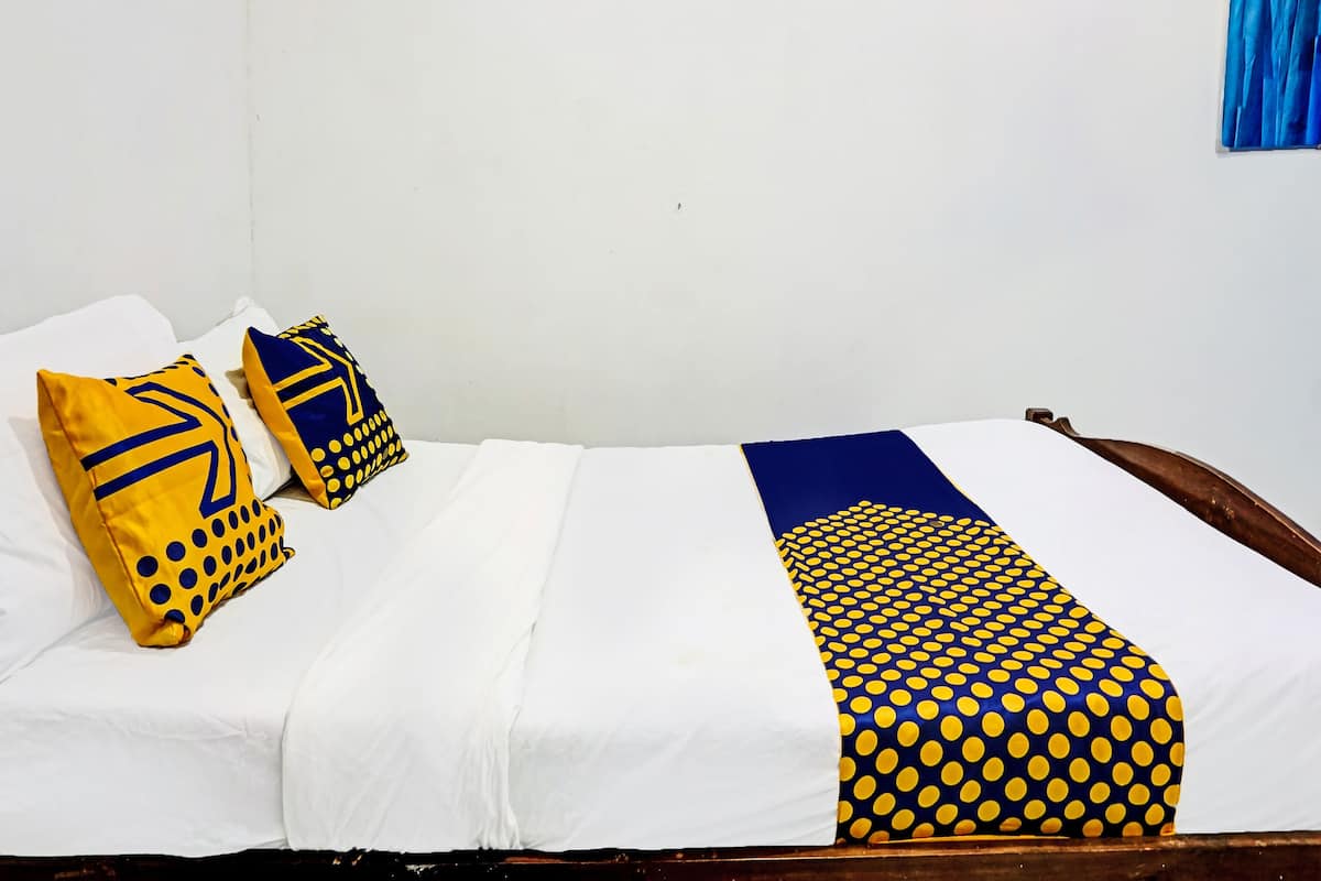 A bed with white bedding, two pillows with yellow and blue patterns, and a blue curtain on the wall.