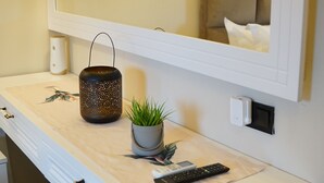 A bathroom with a white vanity, a mirror, a wall-mounted light, a small potted plant, a decorative lantern, and a remote control. - Disa Hotel (Cesme)