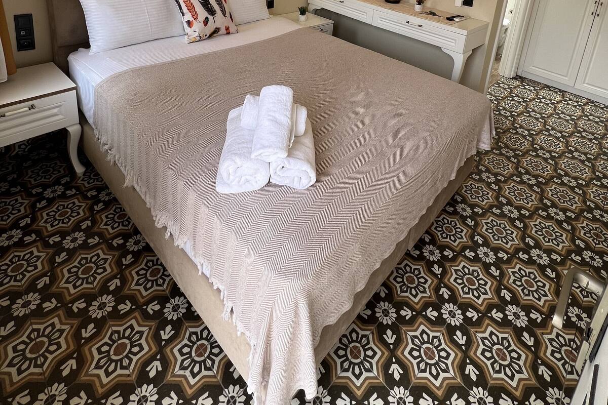 Une chambre d’hôtel bien aménagée, avec un grand lit, une table de chevet, une commode, un miroir et un sol à motifs.