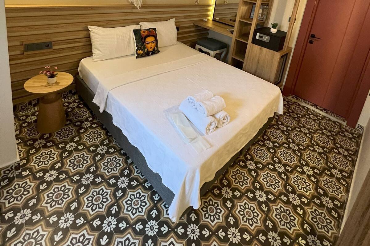 Une chambre d’hôtel comprenant un lit, une table de chevet, un attrape-rêves fixé au mur, un miroir, une armoire et un sol à motifs.