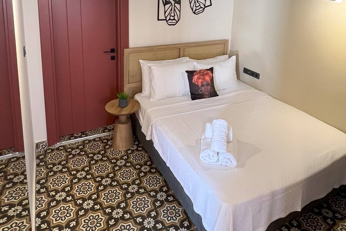 Une chambre d’hôtel avec un lit, une table de chevet, une porte rouge et un sol à motifs.