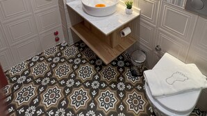 A bathroom with a striped wallpaper, a white sink with a mirror above it, and a patterned floor. - Disa Hotel (Cesme)