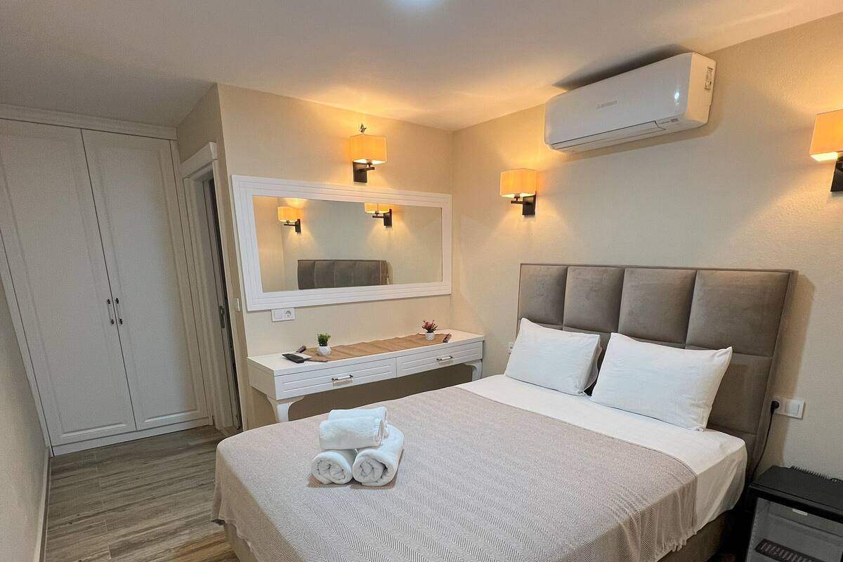 Une chambre à coucher comprenant un lit, des tables de chevet, un miroir et un appareil de climatisation.