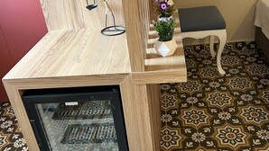 A room with a wooden cabinet, a small refrigerator, a white bench, and a patterned floor. - Disa Hotel (Cesme)