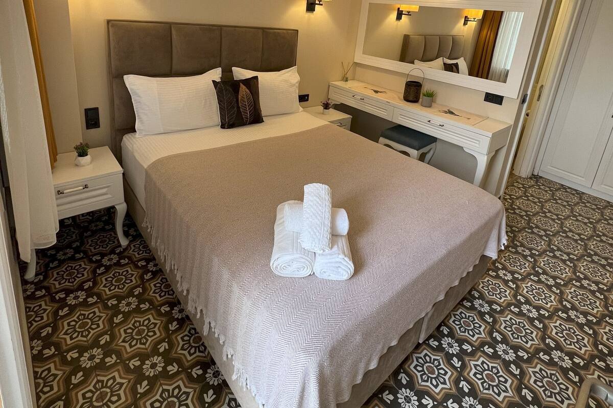 Une chambre d’hôtel comprenant un lit, des tables de chevet, une commode, un miroir et un revêtement de sol à motifs.