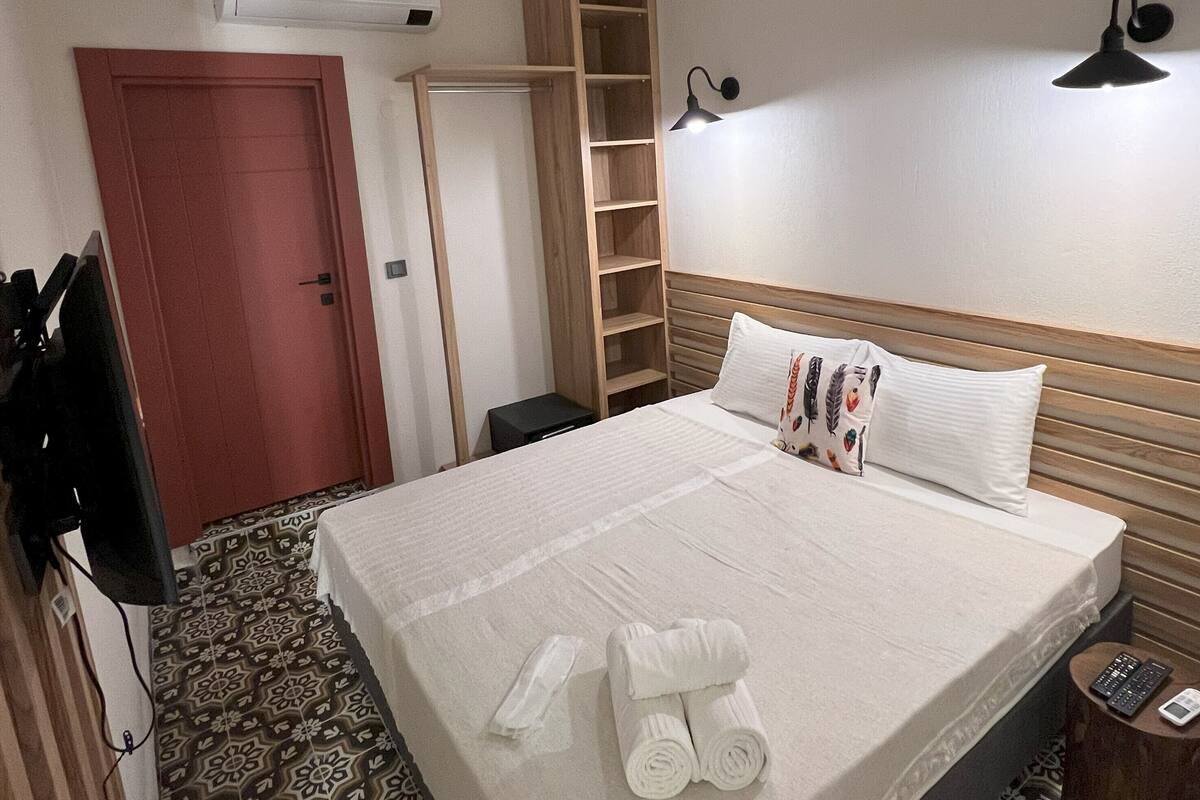 Une chambre d’hôtel avec un lit, une armoire, une télévision, un bureau et un sol à motifs.