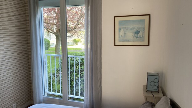 Une chambre à coucher avec un lit, une fenêtre avec des rideaux, un tableau encadré au mur et une table de chevet avec une horloge.