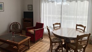 Un coin repas avec une table ronde et des chaises, un fauteuil rouge, un meuble en bois et un téléviseur posé sur un meuble.