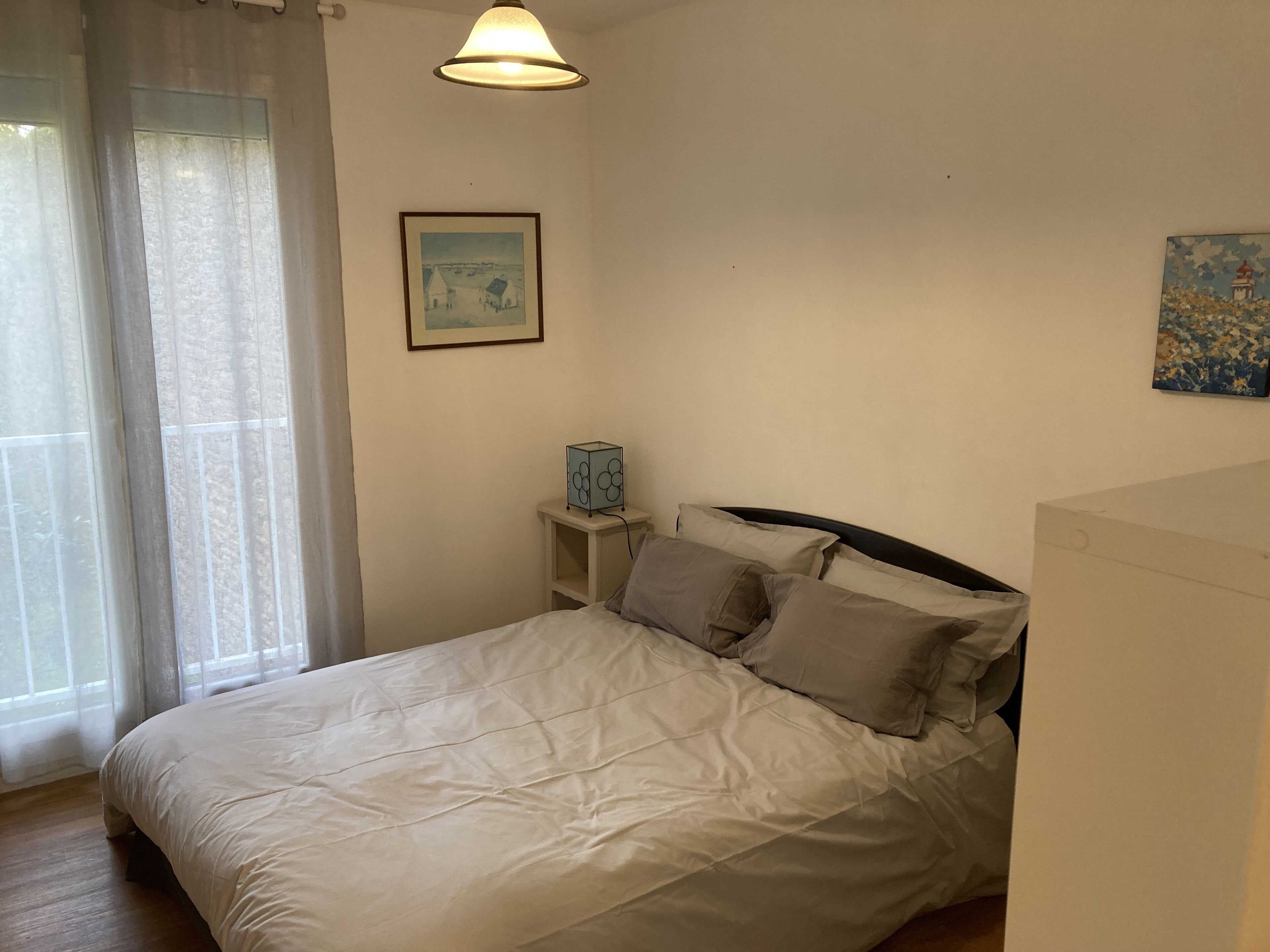 Een slaapkamer met een bed, nachtkastje, lamp en een schilderij aan de muur.