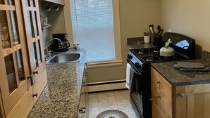 A compact kitchen with a gas stove, a coffee maker, and wooden cabinets. - 2-Bedroom Apt Sleeps 7! - 1/4 mile to Beach! (Hampton)
