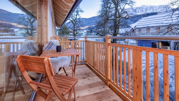 Eine Holzterrasse mit Tisch und Stühlen mit Blick auf eine verschneite Landschaft und Berge.