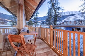 Une terrasse en bois avec une table et des chaises, donnant sur un paysage enneigé et des montagnes.