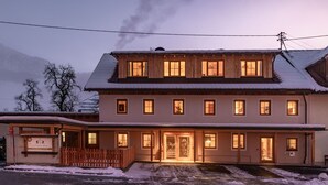 Ein zweistöckiges Holzhaus mit schneebedecktem Dach und einem Holzzaun davor.