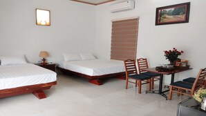 Une chambre d’hôtel avec deux lits, une table à manger avec des chaises, une petite table sur laquelle est posé un vase de fleurs, et un tableau accroché au mur.
