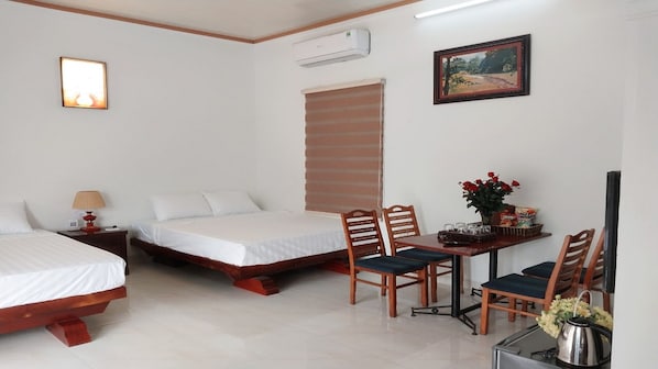 Habitación de hotel con dos camas, un escritorio con sillas, un televisor y un cuadro en la pared.
