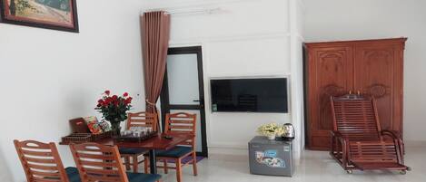 Un comedor con una mesa, sillas, un jarrón de flores rojas, un refrigerador pequeño y un mueble de madera.