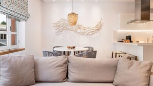 A modern living room with a sofa, a dining table, and chairs. There is a decorative wall piece above the table and a kitchen area with a stove and cabinets.