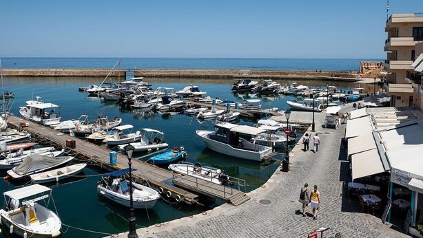A marina with various boats docked, a cobblestone walkway, and a building with outdoor seating.