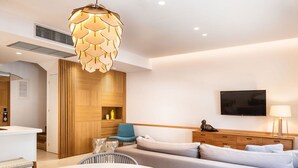 A modern living room with a sofa, a dining table with bowls, a television, and a unique pendant light.
