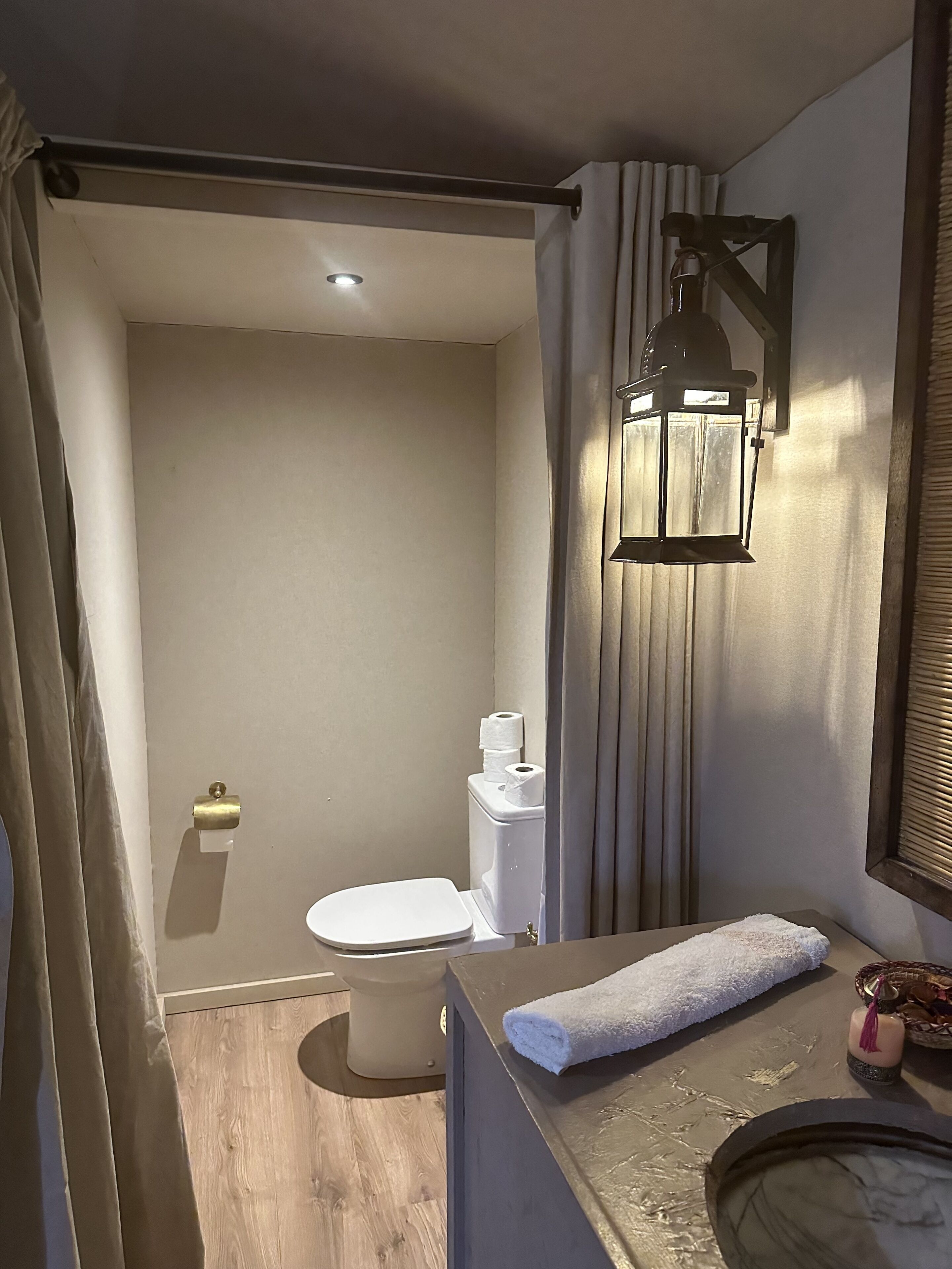 A compact bathroom with a toilet, a towel, a small sink, and a wall-mounted light fixture.