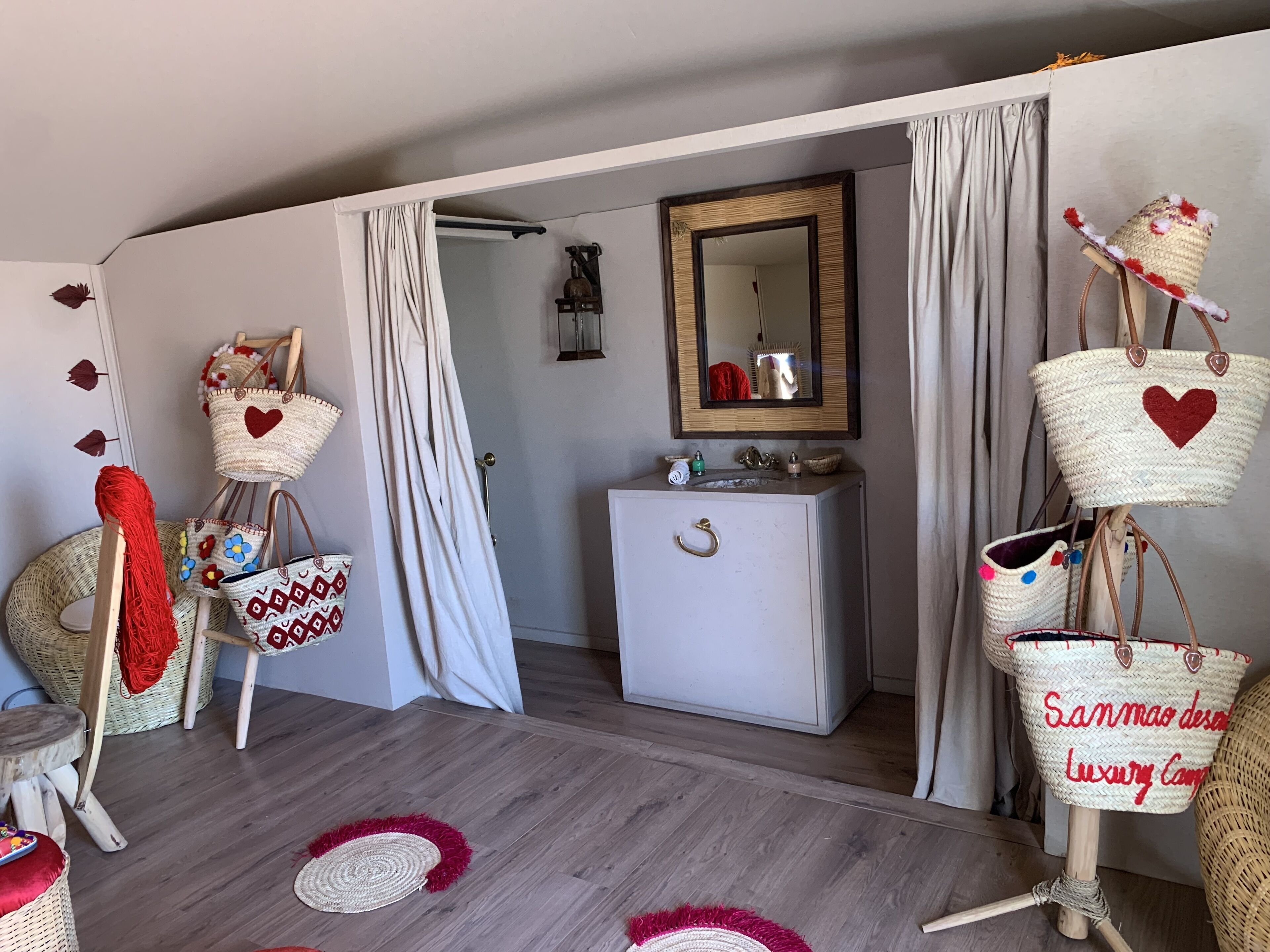 Una habitación con piso de madera, un tocador blanco con espejo y varias cestas de mimbre con diseños de corazones.