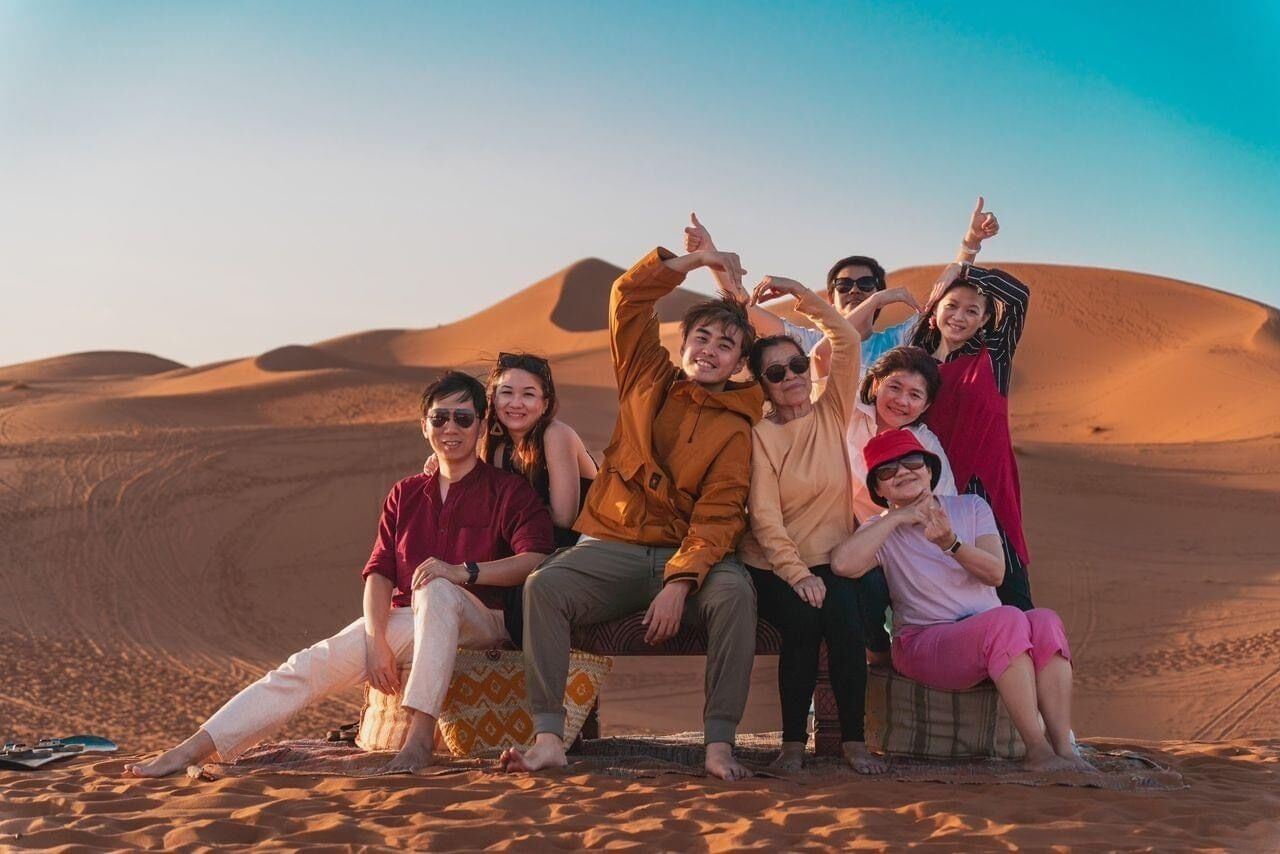 A group of people sitting on a dune in a desert landscape.