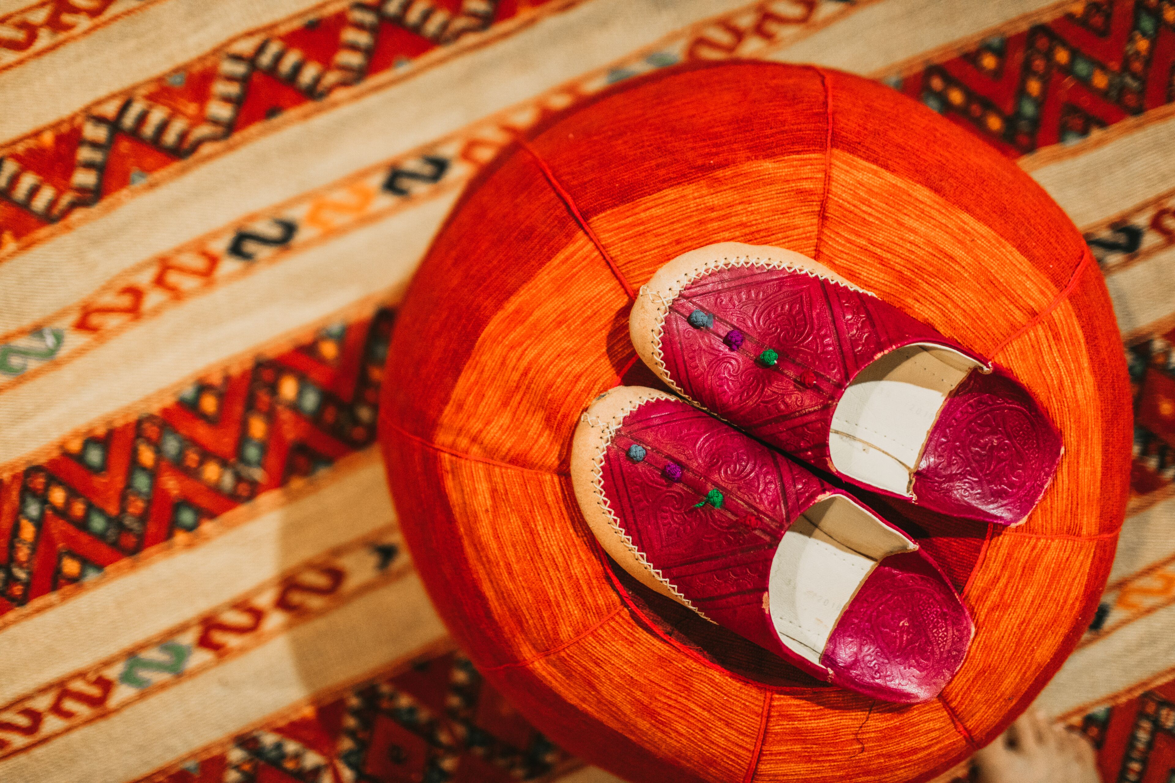 A pair of red embroidered slippers on a round wooden tray.