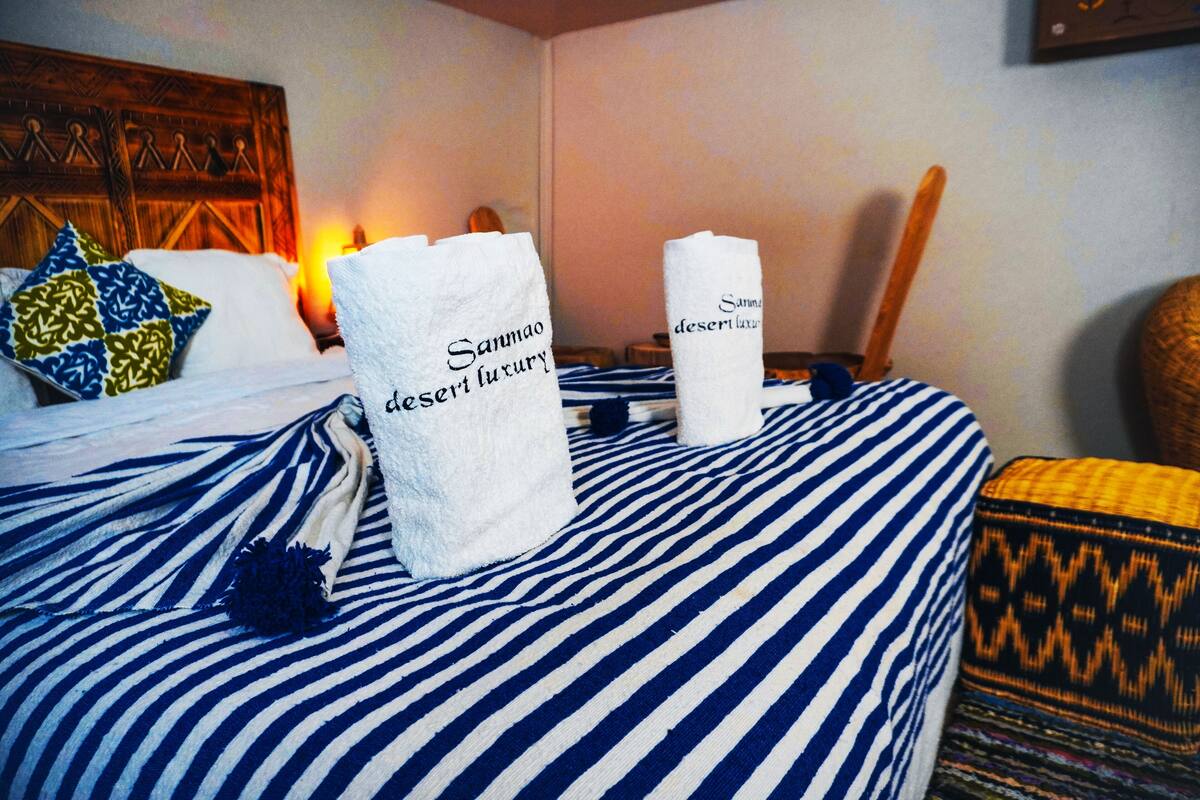 A hotel room with a bed featuring striped bedding, a decorative pillow, and two towels with the text "Sannmo desert luxury".