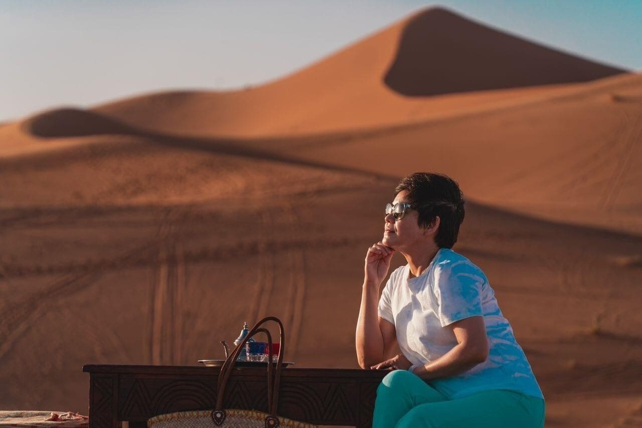 A person sitting on a bed with a view of sand dunes in the background.