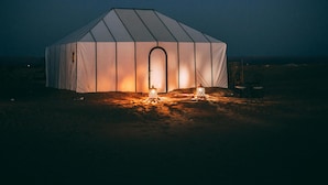 A large, white, dome-shaped tent with a central door, illuminated by a warm light source inside.
