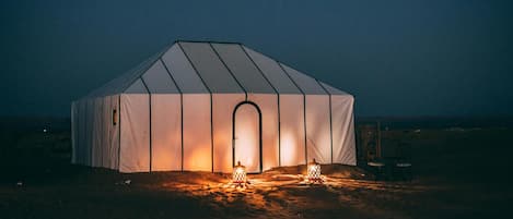 A large, white, dome-shaped tent with a central door, illuminated by a warm light source inside.