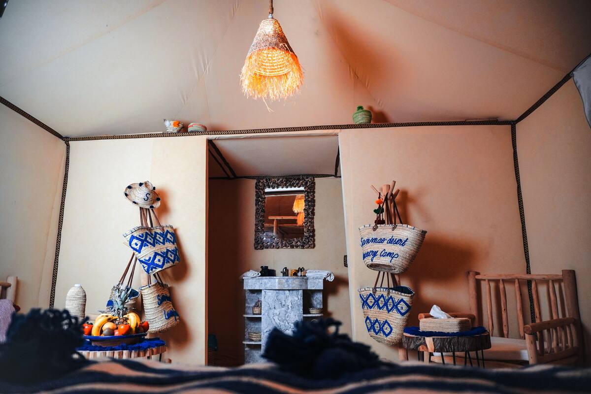 A cozy room with a hanging light fixture, a mirror, and a small table with fruits and woven bags.