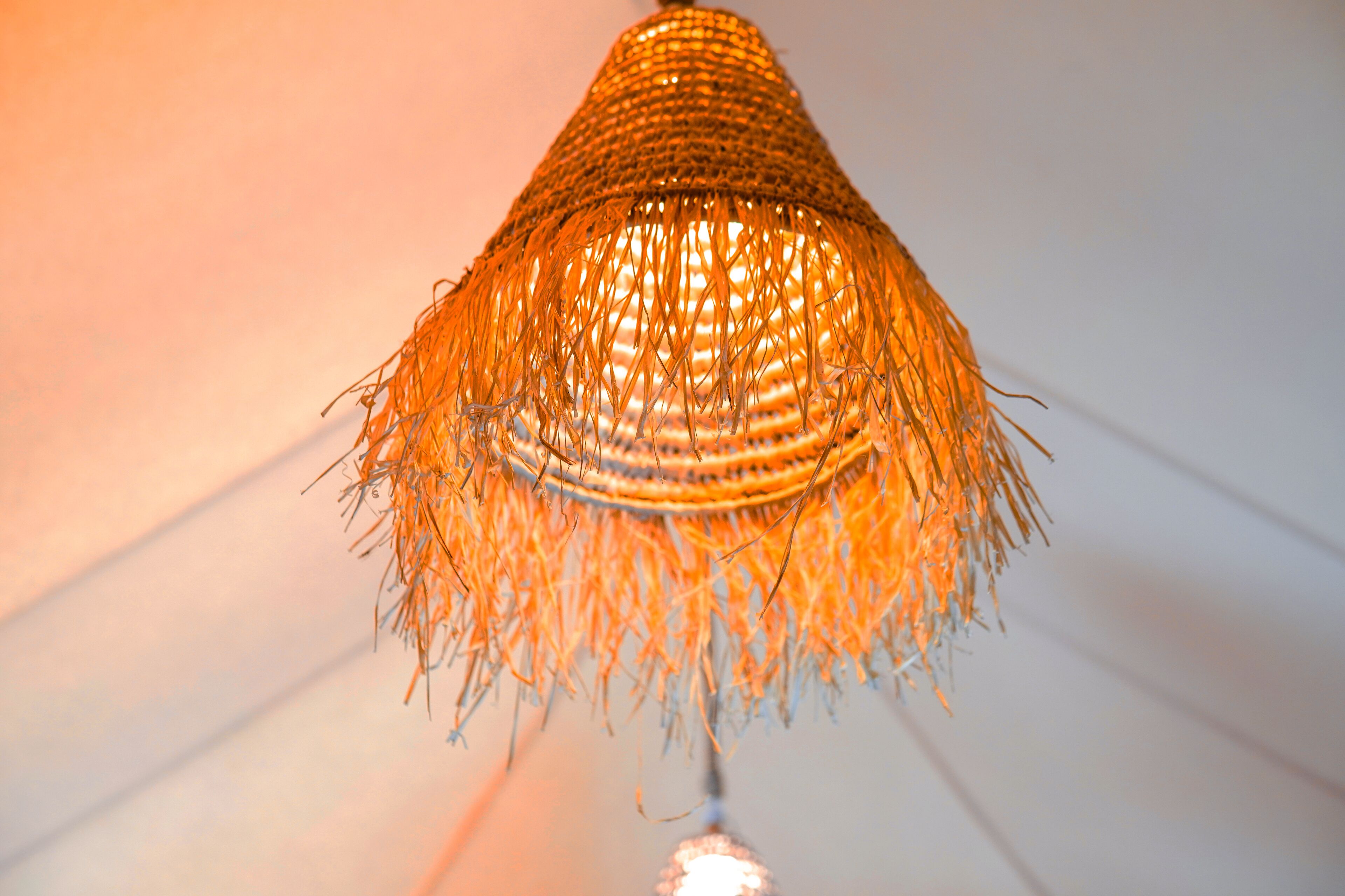 A close-up of a woven, conical light fixture with a warm glow.