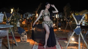 A person seated on a camel in a desert setting with traditional tents and lanterns.