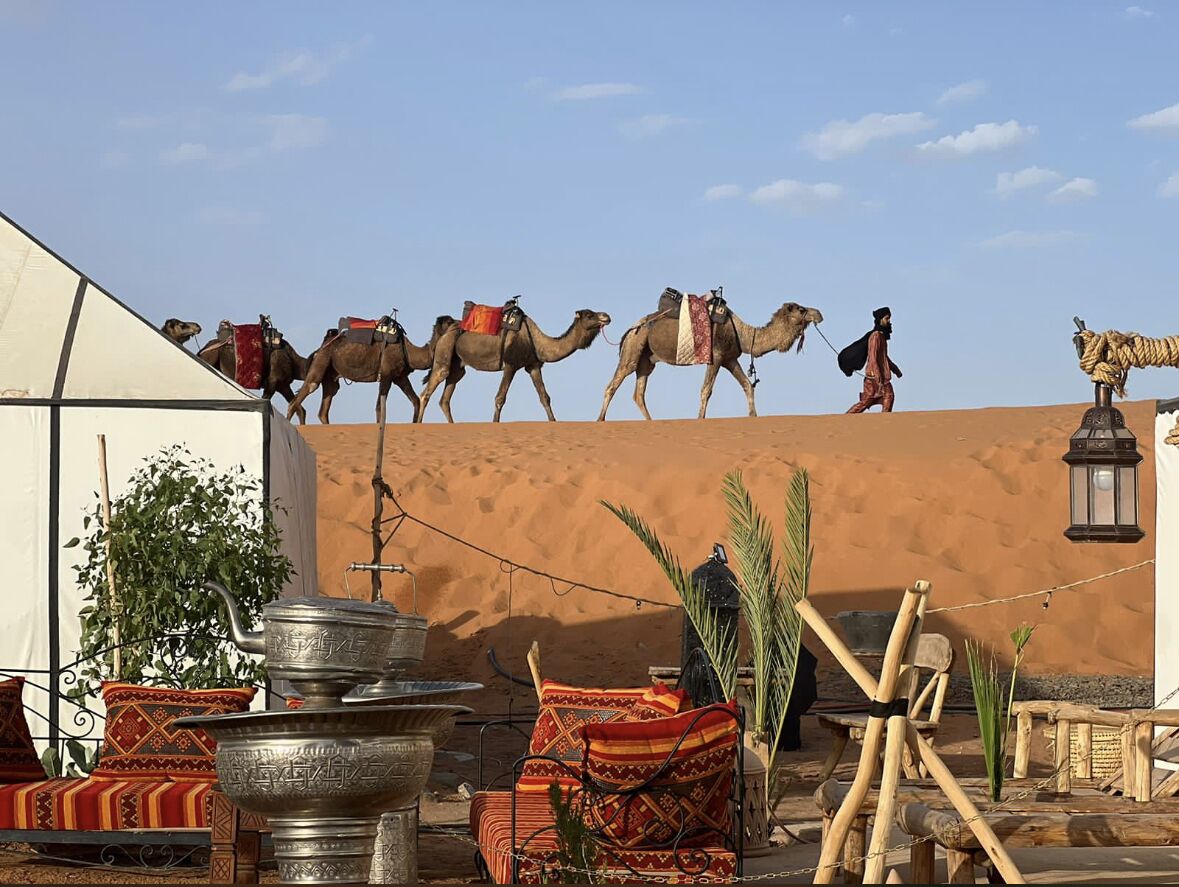 Escena desértica con camellos, una tienda de campaña y mobiliario tradicional.