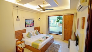 A bedroom with a bed, bedside tables, a ceiling fan, a window with a view, and a door. - Maharaja Palace Near Medanta Gurgaon  (Gurugram)