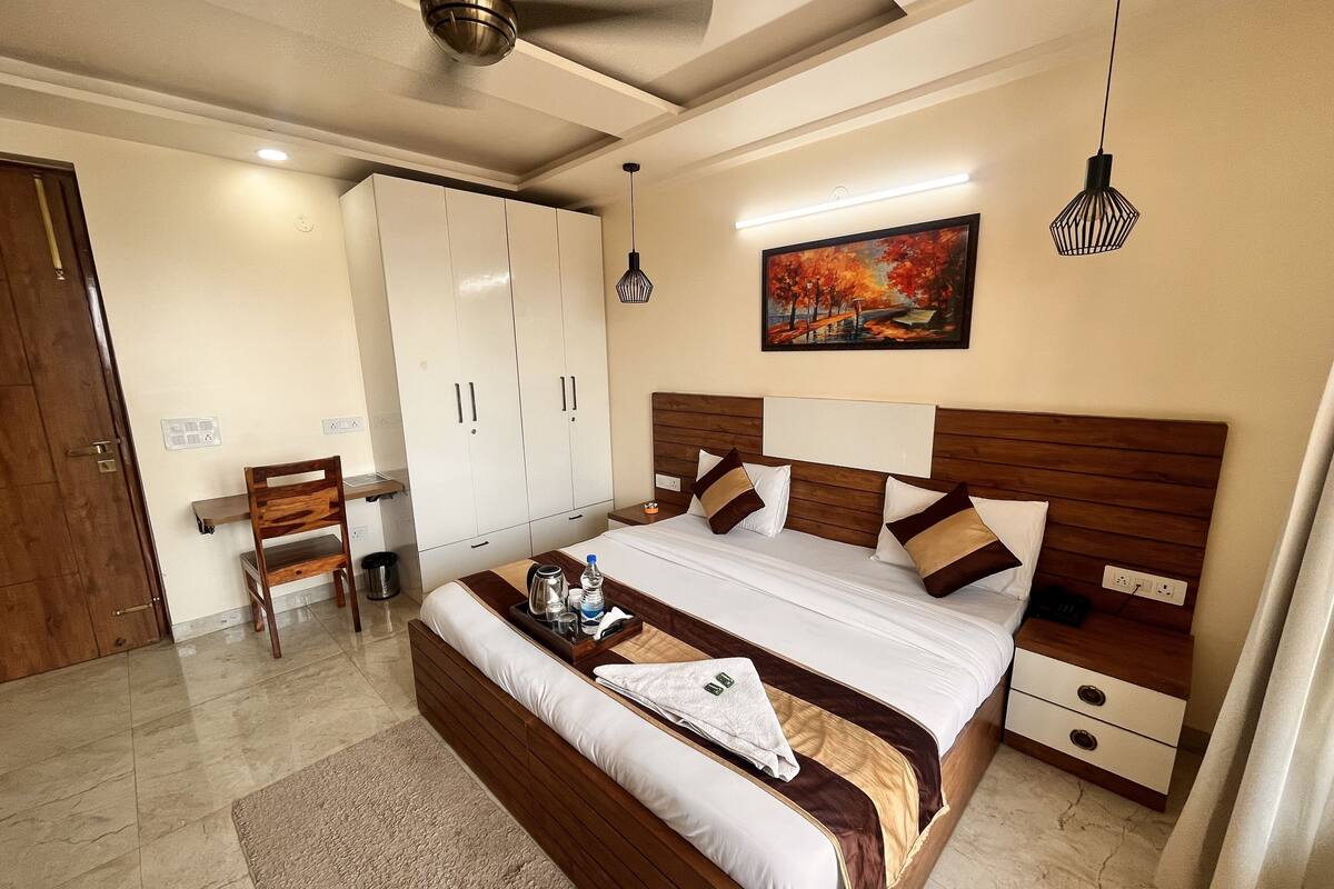 A hotel room with a bed, bedside tables, a desk, a chair, a wardrobe, and a painting on the wall.