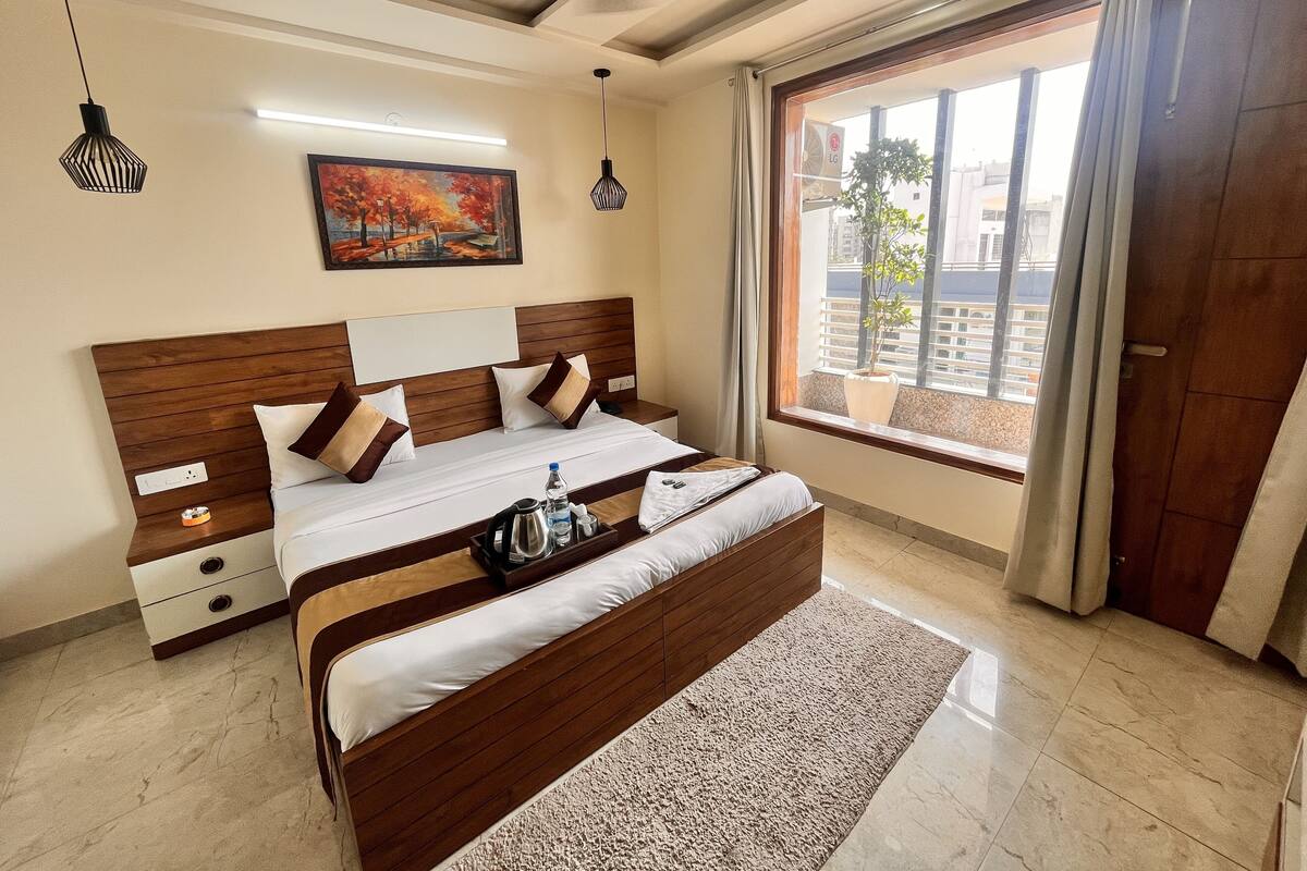 A hotel room with a large bed, a painting on the wall, a window with a view, and a ceiling light.