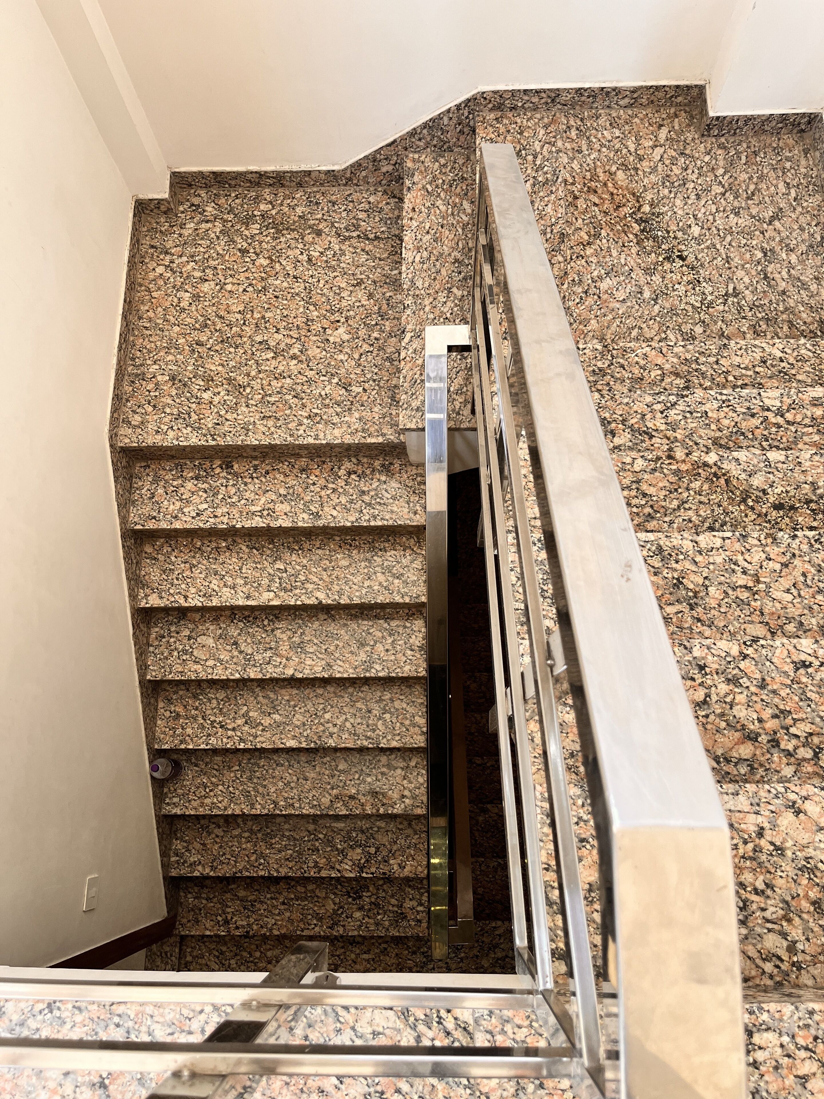 Un escalier avec des marches en granit et une rampe métallique.