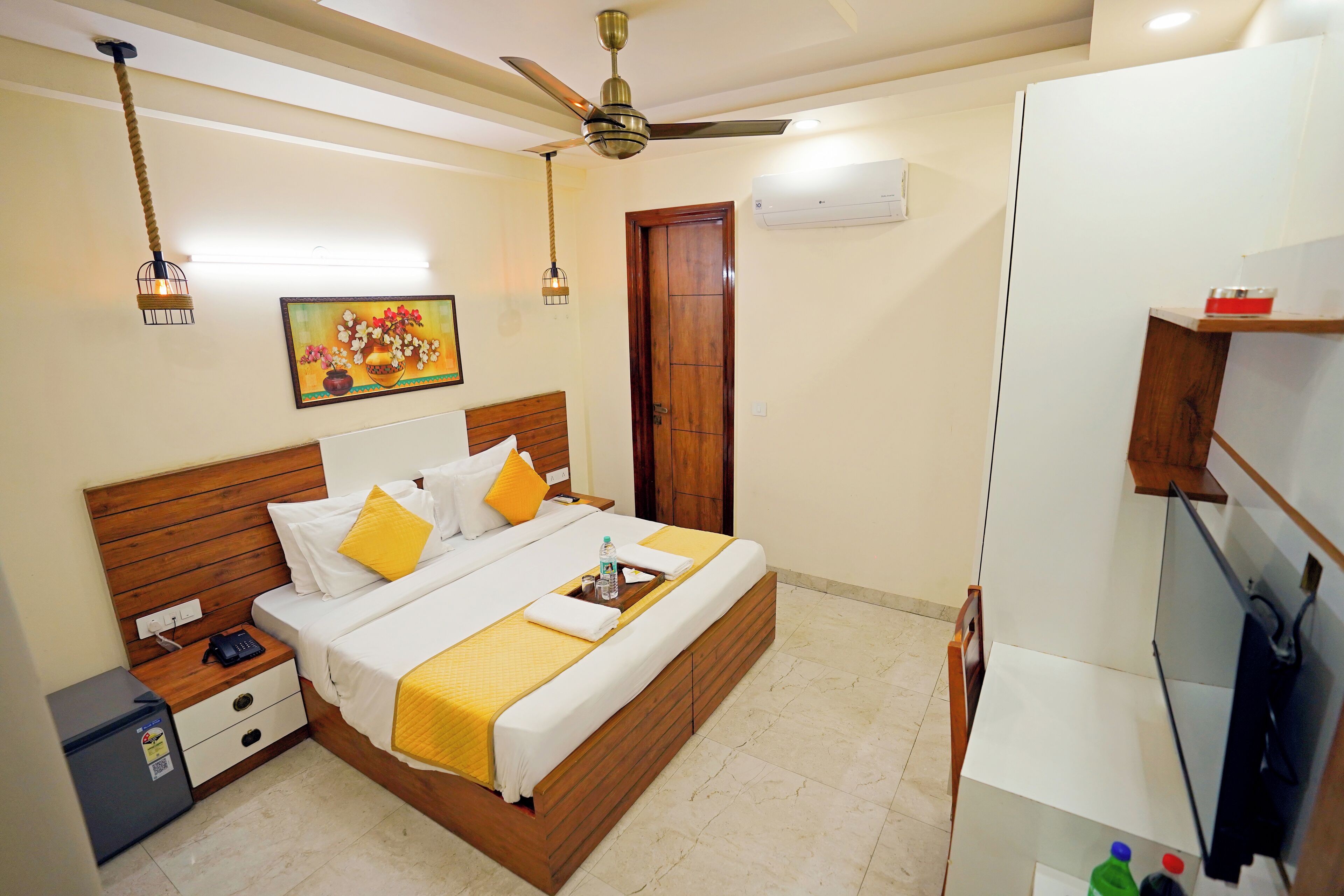 A neatly arranged hotel room with a wooden bed, a small desk, a ceiling fan, and a television.