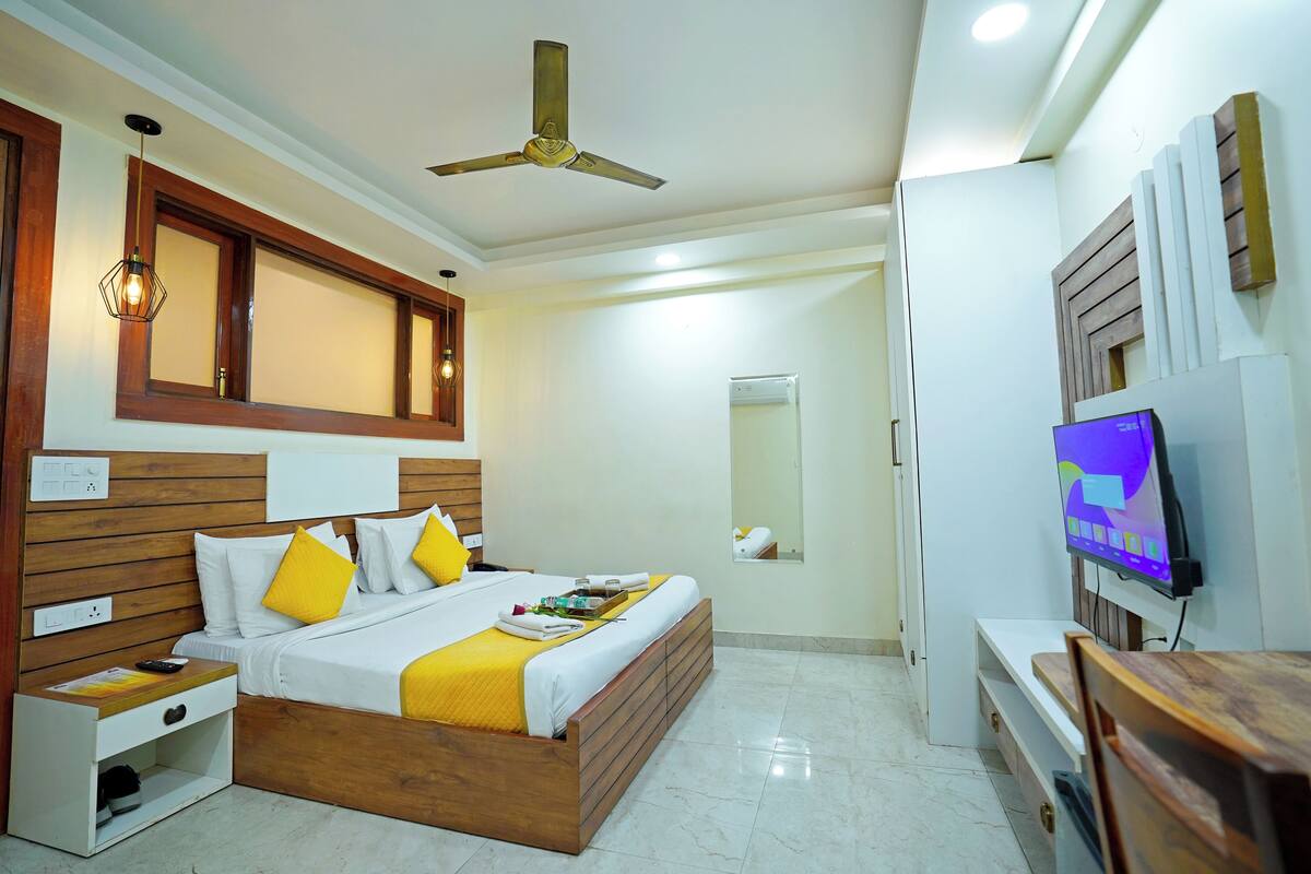 A modern hotel room with a wooden bed, a ceiling fan, a TV, and a mirror.