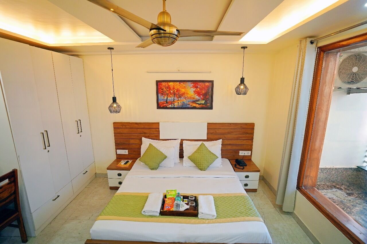 Habitación de hotel con una cama, cabecera de madera, mesitas de noche, ventilador de techo, un cuadro y una ventana con vistas.