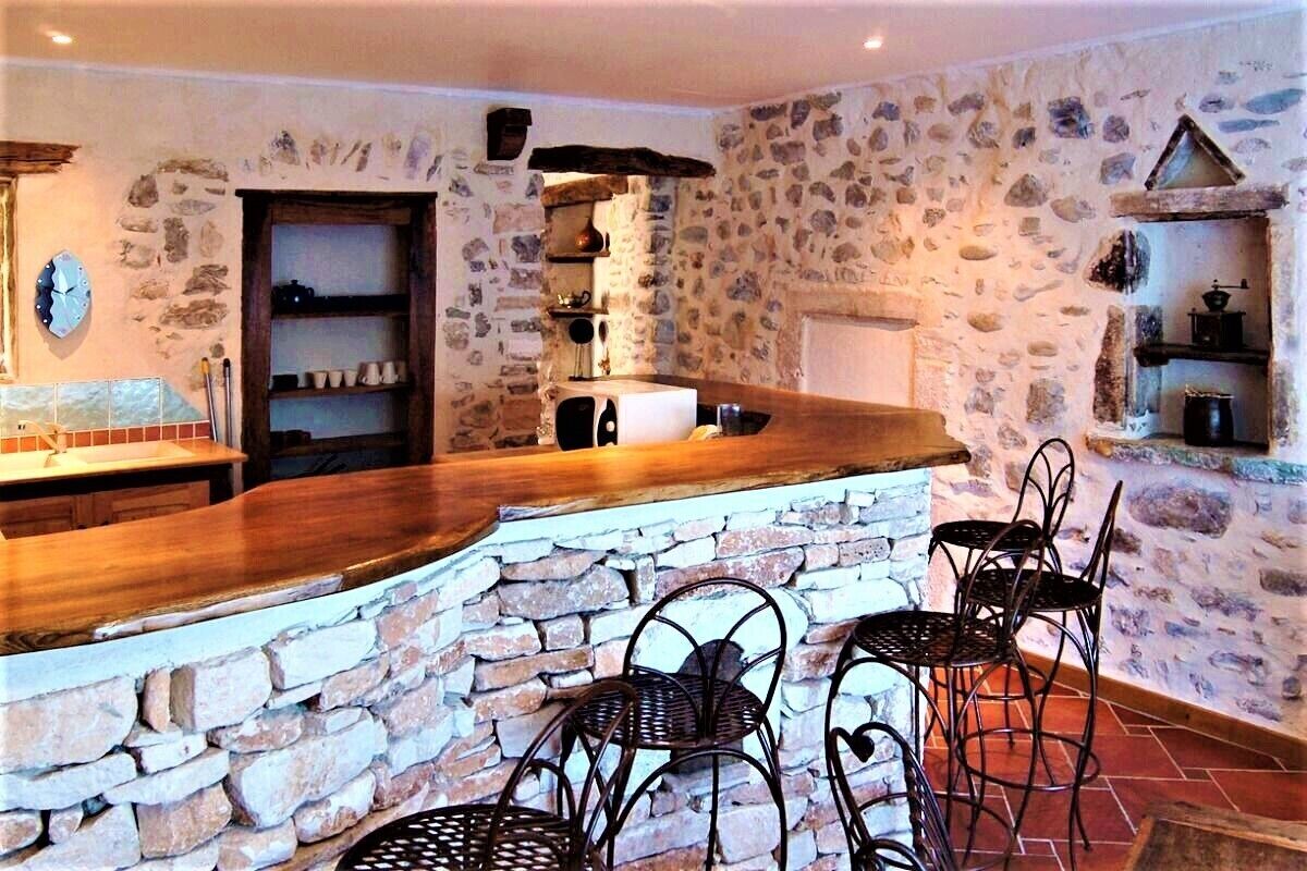 Una cucina rustica con pareti in pietra, un bancone in legno e sedie in metallo.