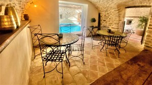 A stone-walled dining area with a pool view, metal chairs, and a table with a patterned tablecloth. - Gîte 4* for 6p, 3ch, 100m2, HEATED SWIMMING POOL, PATIO (Vallon pont d'arc)