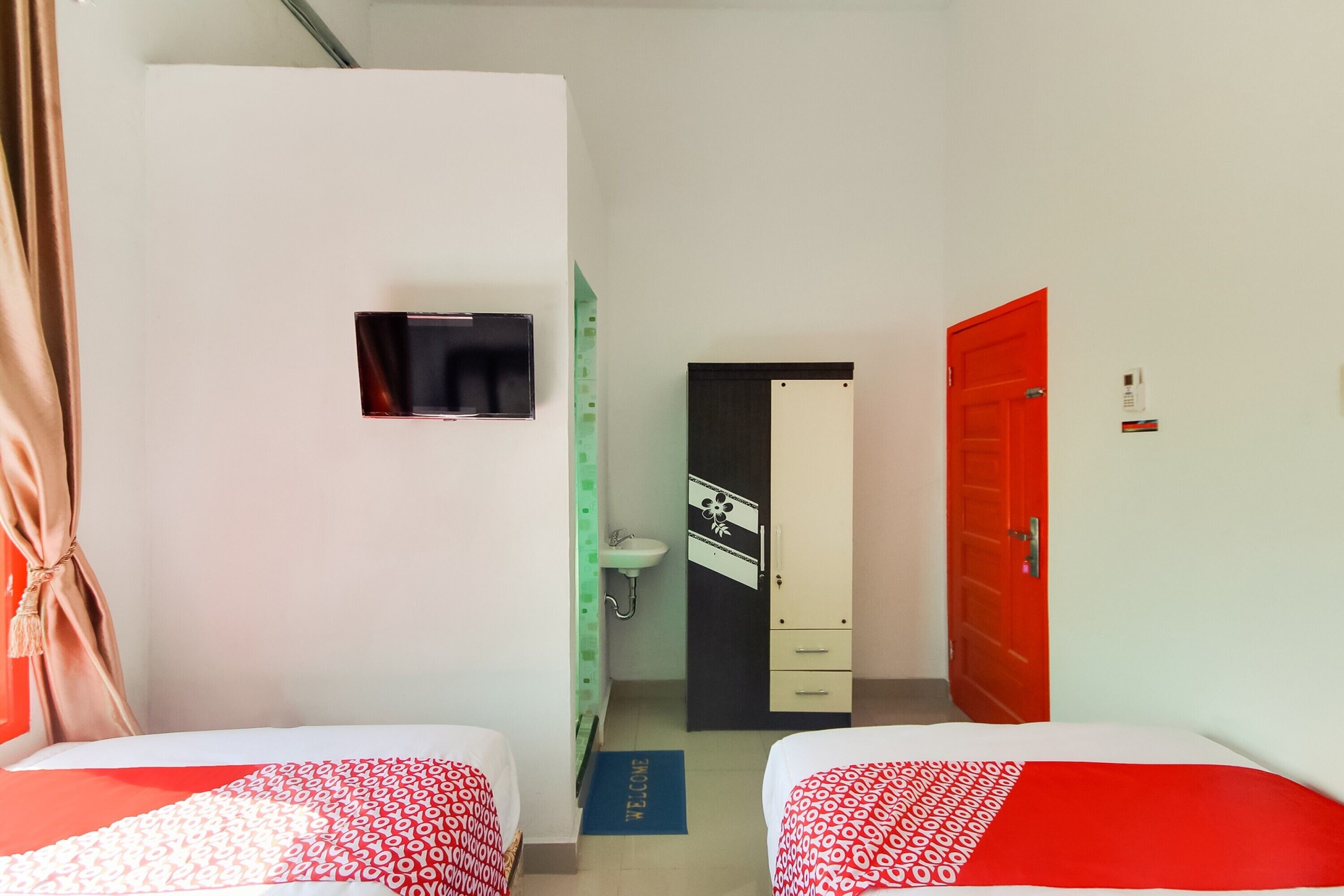 Una habitación de hotel con dos camas, televisión, armario, lavabo y una puerta roja.