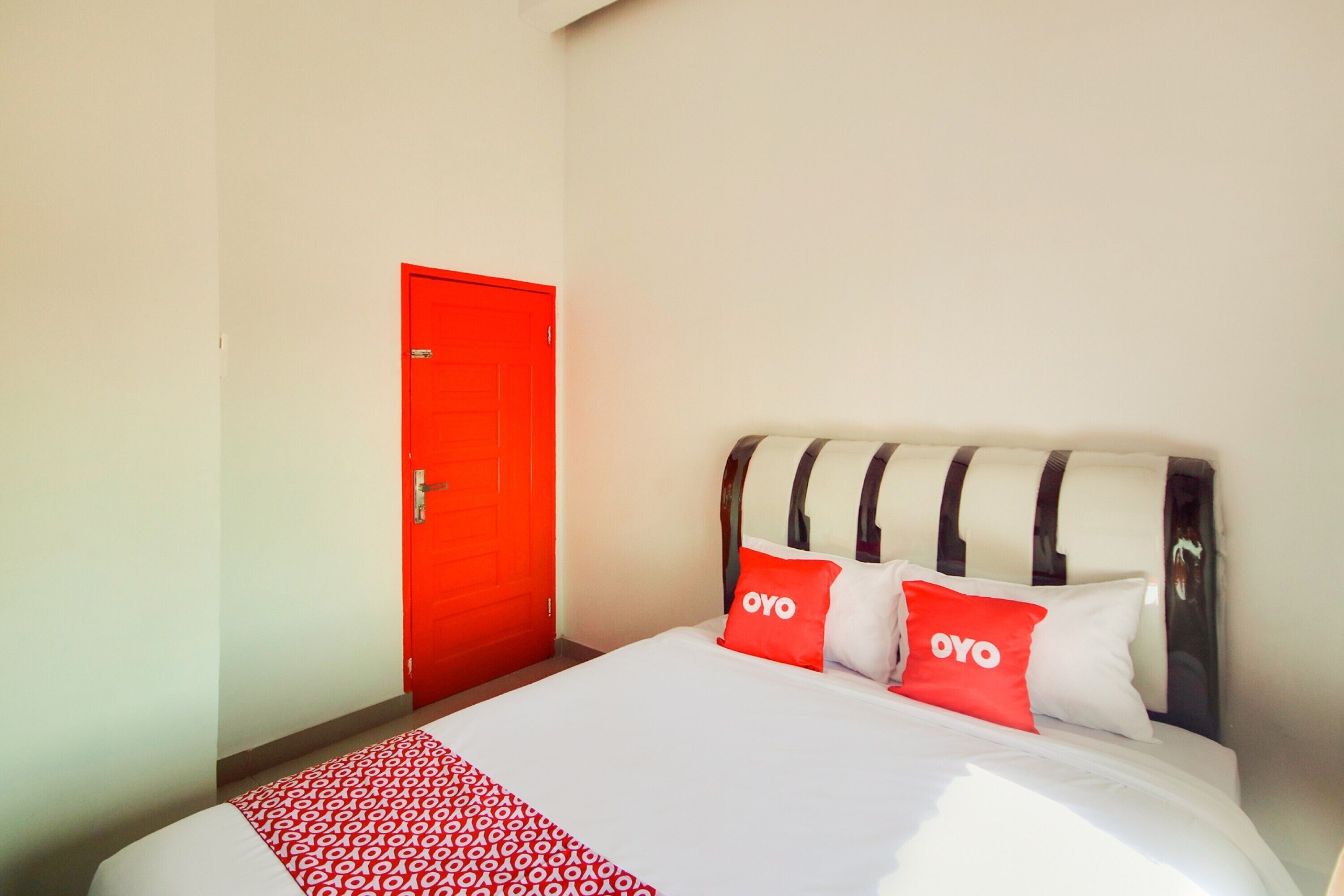 A hotel room with a bed, a red door, and two pillows with the logo "OYO".